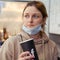 Woman in medical mask drinks coffee from paper cup. An adult woman looks at the cafes opened after the coronavirus quarantine