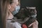 A woman in a medical mask holds a British cat in her arms. the cat is also in a medical mask