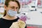 A woman in a medical mask holds a euros, background of a store. A customer in a medical mask stands in a supermarket with money in