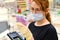 Woman in medical mask holds money euro near the cash desk of the store. A cashier counts money against the background of a