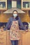 Woman in medical mask in the kitchen. Beautiful woman in medical maskin an apron standing in kitchen. toned. vertical photo