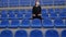 Woman in medical mask sits on stadium bleachers alone, roots for her favorite sports team and resents by game\'s progress