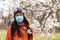 A woman in a medical mask stands on the street near a flowering tree. Concept of seasonal pollen Allergy and viral infections