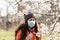 A woman in a medical mask stands on the street near a flowering tree and tries to smell the flowers. Concept of seasonal pollen