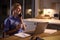 Woman In Medical Scrubs Talking On Mobile Phone Working Or Studying On Laptop At Home At Night