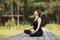 A woman meditates in a lotus position on a wooden walkway on a summer sunny morning