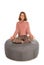Woman meditates while sitting in the lotus position on round shape grey beanbag chair