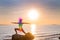 Woman is meditating with glowing seven chakras on the beach. Silhouette of woman is practicing yoga at sunset on stone