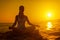 Woman meditating in lotus pose at sunset