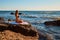 Woman meditating in lotus position. Female enjoying ocean view sitting on rock. Yoga and pilates concept, copy space