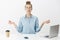 Woman meditating in office sitting near table having break from writing article in laptop, drinking coffee looking up