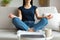 Woman Meditating Sitting In Lotus Position On Couch Indoor, Cropped