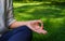 A woman is meditating under the shade sitting cross-legged on green grass in the shade of trees at lunchtime. Hand lying on a knee