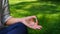 A woman is meditating under the shade sitting cross-legged on green grass in the shade of trees at lunchtime. Hand lying on a knee