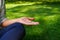 A woman is meditating under the shade sitting cross-legged on green grass in the shade of trees at lunchtime. Hand lying on a knee