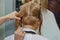 Woman with medium long blonde hair. With a short haircut at the hairdresser at the stylist using scissors. Care procedures. The