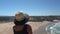 Woman in a middle-aged hat stands on a mountain slope and admires the beautiful view of the Portuguese beach Odeceixe in