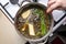 The woman mixes the mushroom soup with a metal spoon which is in a metal pot on the gas stove, top view.