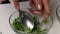 A woman mixes parsley, garlic and salt in a glass container. Salted lard with herbs and spices