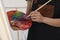 Woman mixing paints on palette with brush near easel in studio, closeup