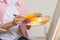 Woman mixing paints on palette near easel in studio, closeup