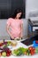 Woman mixing salad while cooking with laptop in kitchen