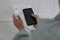 Woman with mobile phone plugging charger in socket on white brick wall, closeup