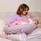 Woman mother breastfeeds an infant baby sitting on a home sofa. Mom feeds milk toddler baby in living room