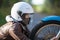 Woman in a motorcycle helmet clutching motorbike spoked wheel looks at a headlight