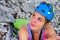 Woman mountaineer with helmet and backpack, sitting down, resting and looking up towards a rock climbing wall
