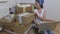 Woman on moving day sitting on floor among cardboard boxes and using laptop