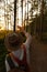 Woman naturalist in hat and orange overalls with backpack looking at the sun through her fingers at sunset, exploring wildlife and