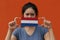 A woman with Netherland flag on hygienic mask in her hand and lifted up the front face on orange color background. Tiny Particle