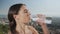 Woman opening bottle with water. Girl drinking water after yoga workout outside