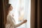 Woman opening elegant window curtains in room