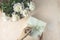 Woman opening her present, top view. Female`s hands pull ribbon to unwrap gift box among the white peony flowers, festive flat la