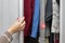 woman opens wardrobe door with clothes with hand.