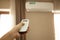 Woman operating remote controller on Air conditioner inside the room.