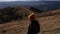 A woman in an orange beanie hat is standing in front of the mountains background