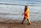 A woman in the orange coat walking on the beach at early spring in Gloucester, Massachusetts