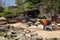 A woman with an orange handkerchief on her shoulders walks along the rocky coast along the village houses in Goa, India