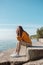 Woman in orange sweater sitting on a stone stairs on a beach with her eyes closed