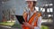 Woman in orange vest and hardhat working on tablet device at construction site