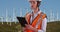 Woman in orange vest and hardhat working on tablet by wind turbines outdoors