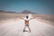 Woman with outstretched arms standing on gravel road crossing the Namib desert, in the Namib Naukluft National Park, main travel