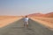 Woman with outstretched arms standing on gravel road crossing the Namib desert, in the Namib Naukluft National Park, main travel d