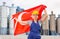 woman in overalls with Turkey flag in her hands against the background of chimneys of modern factory