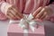 Woman packaging a gift for posting tying a pink ribbon around a giftwrapped box. Generated ai
