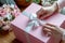 Woman packaging a gift for posting tying a pink ribbon around a giftwrapped box. Generated ai