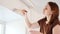 Woman paints with a brush and white paint wall above window. a DIY repair.